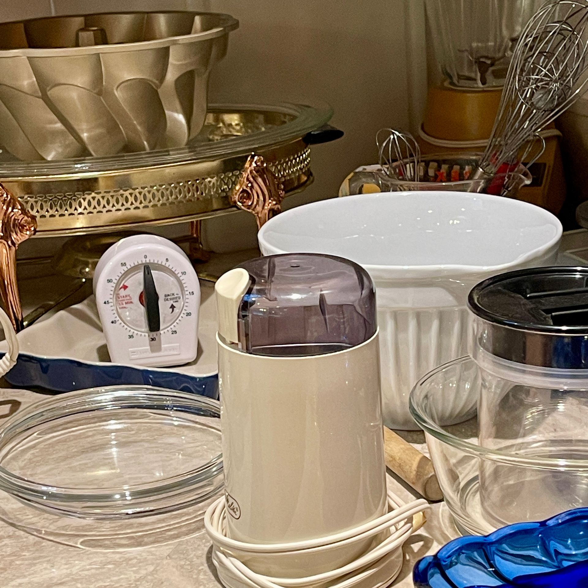 Kitchen countertop with a coffee grinder, bowls, a timer, and baking dishes.