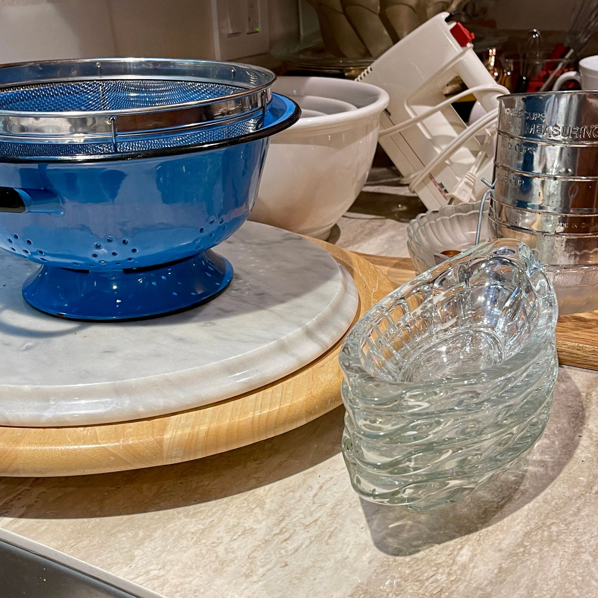 Blue colander, white bowl, glass dishes on a wood surface. Kitchen setting.