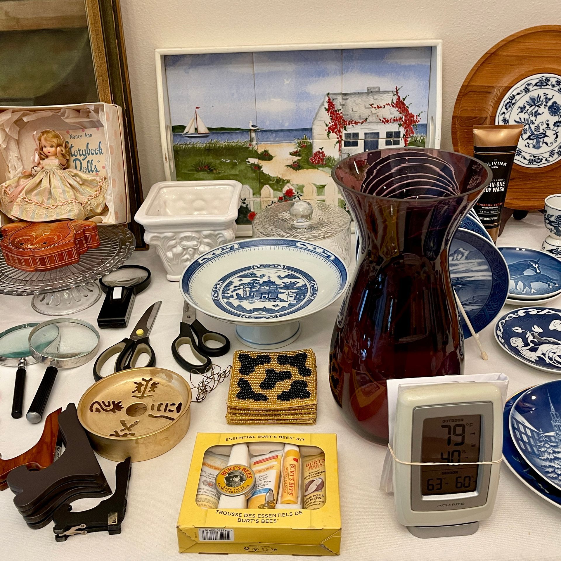 A variety of antique objects on a table. Includes china, a painting, scissors, and a thermometer.