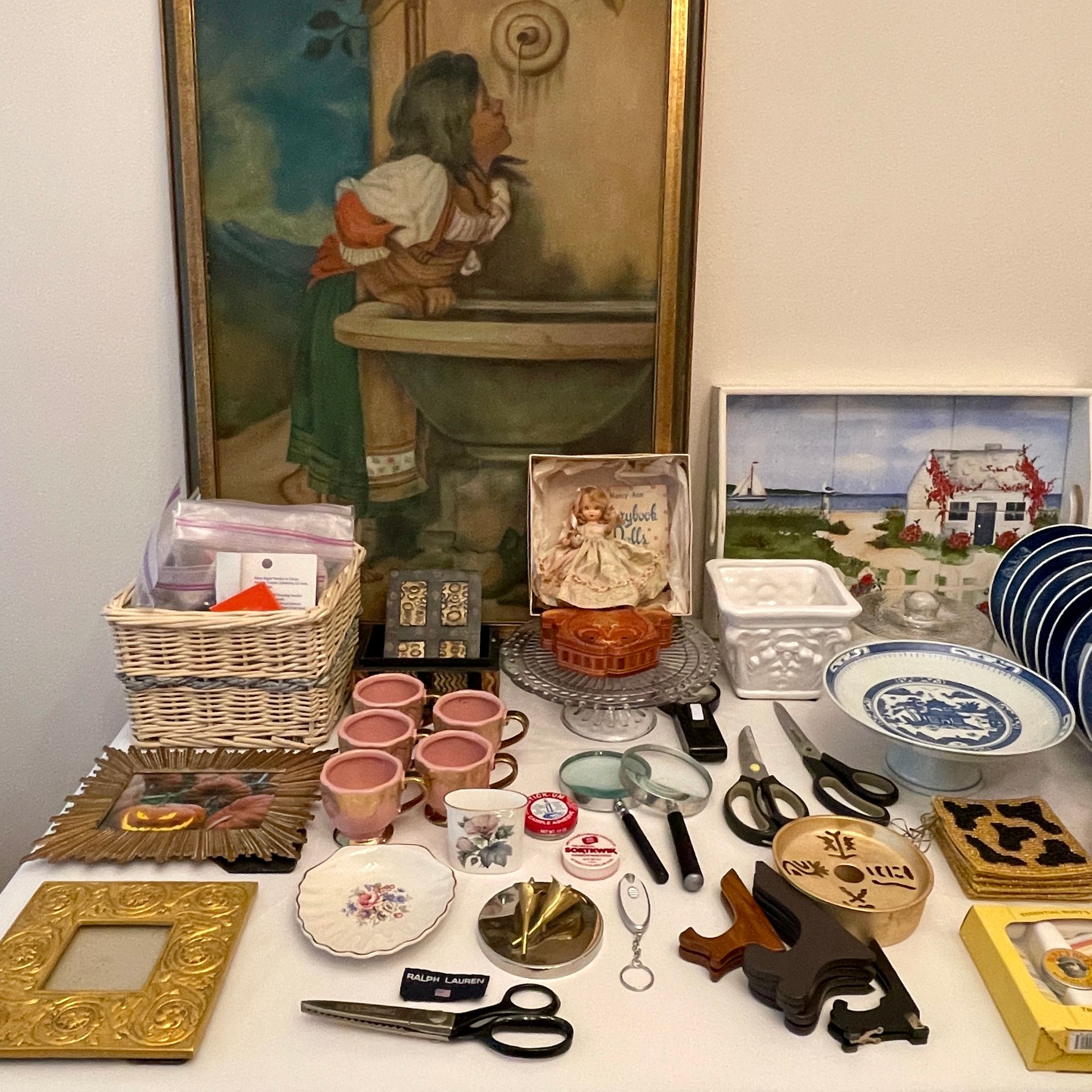 Various vintage items on a white surface: art, dishes, basket, magnifier, scissors, and other collectibles.