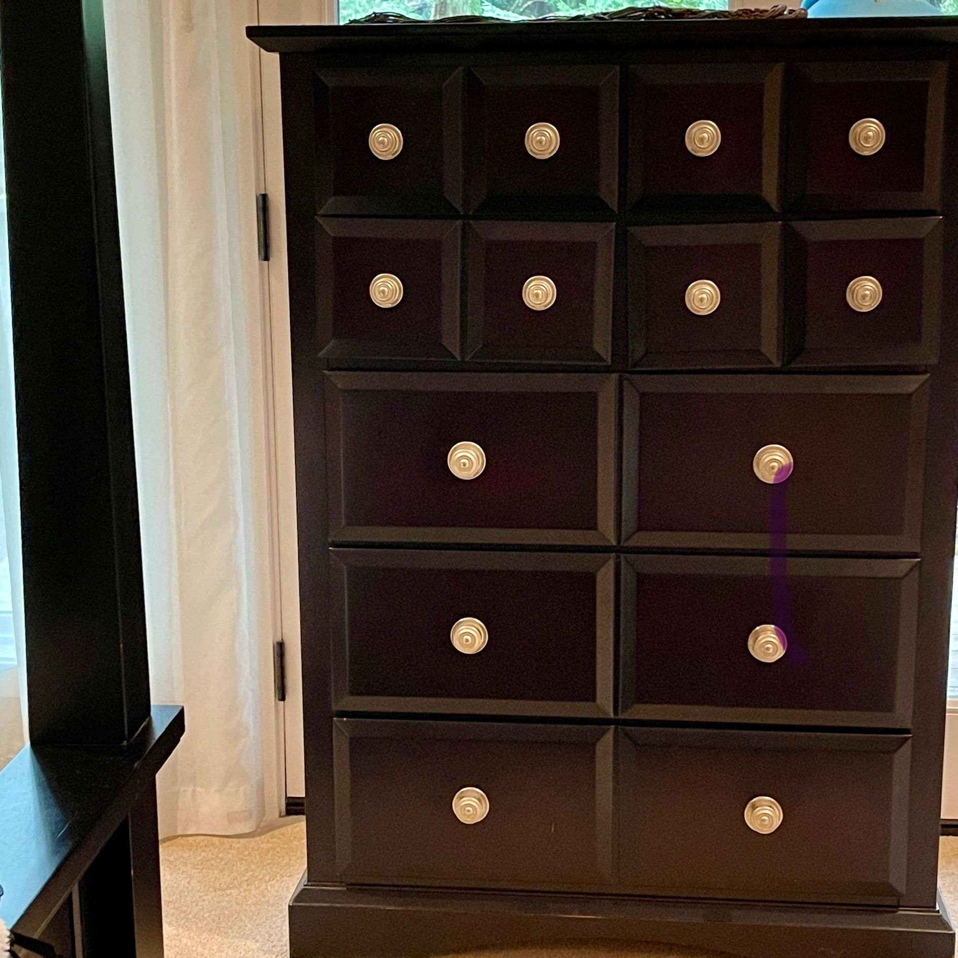 Black dresser with gold knobs, in front of a white curtain.