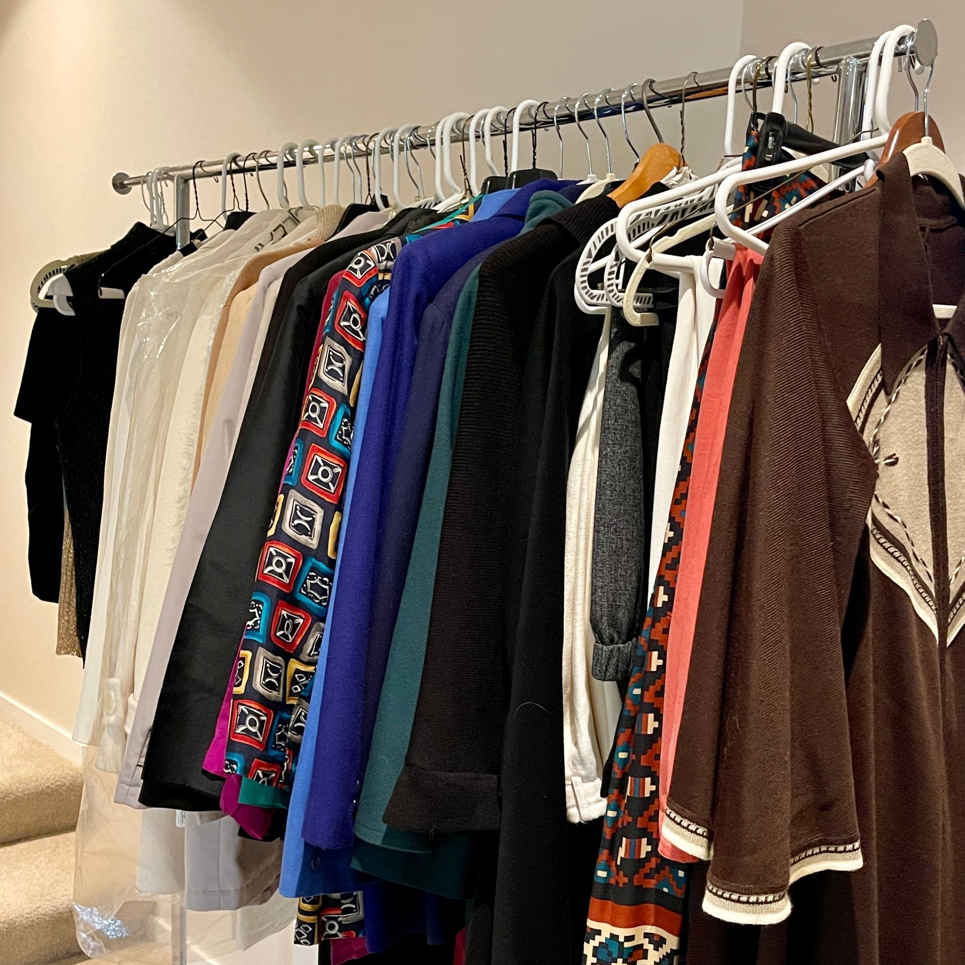 Clothes on hangers, mostly jackets and dresses. Silver rod, white hangers, and variety of colors.