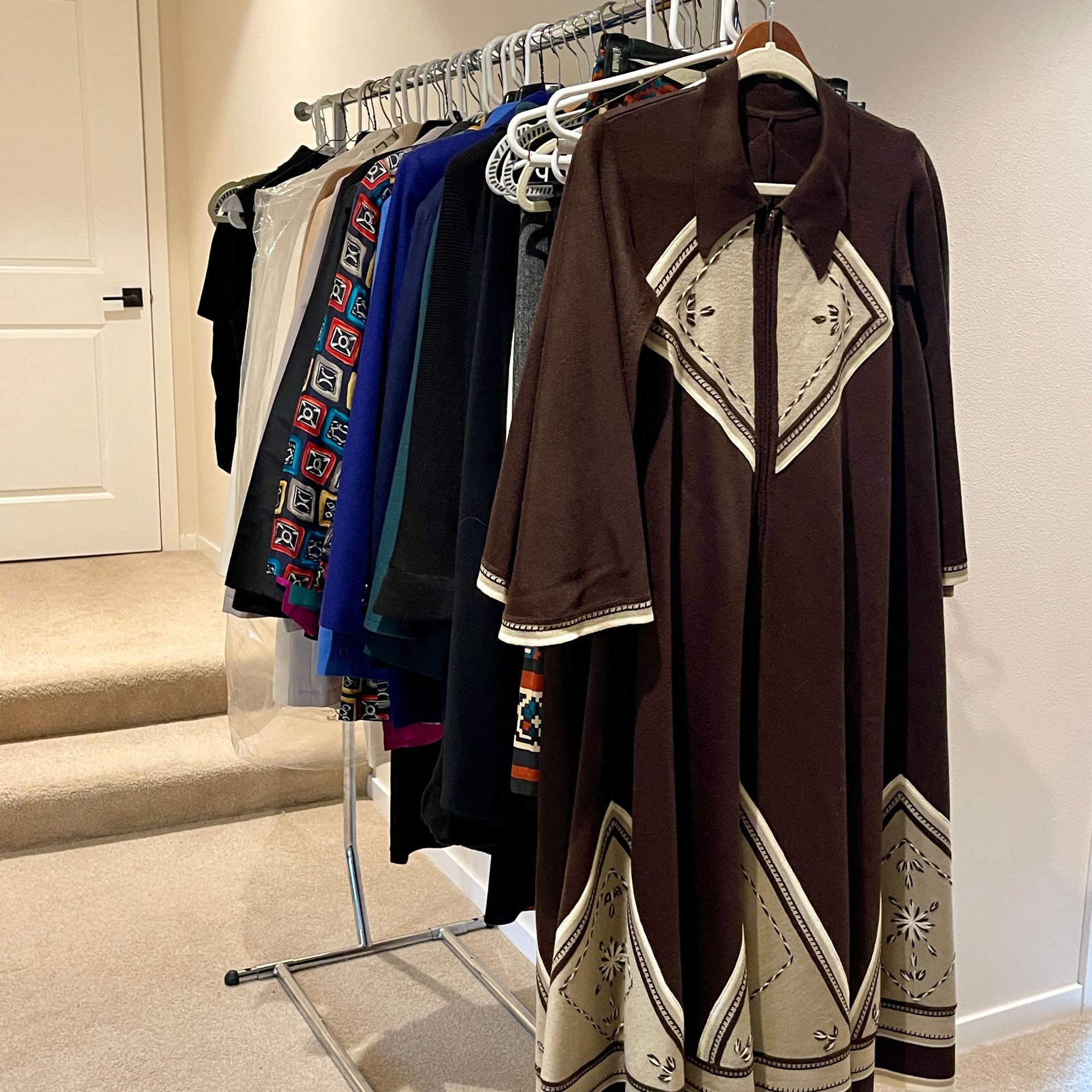Clothing rack with various garments; a long brown dress with cream diamond patterns is prominent.