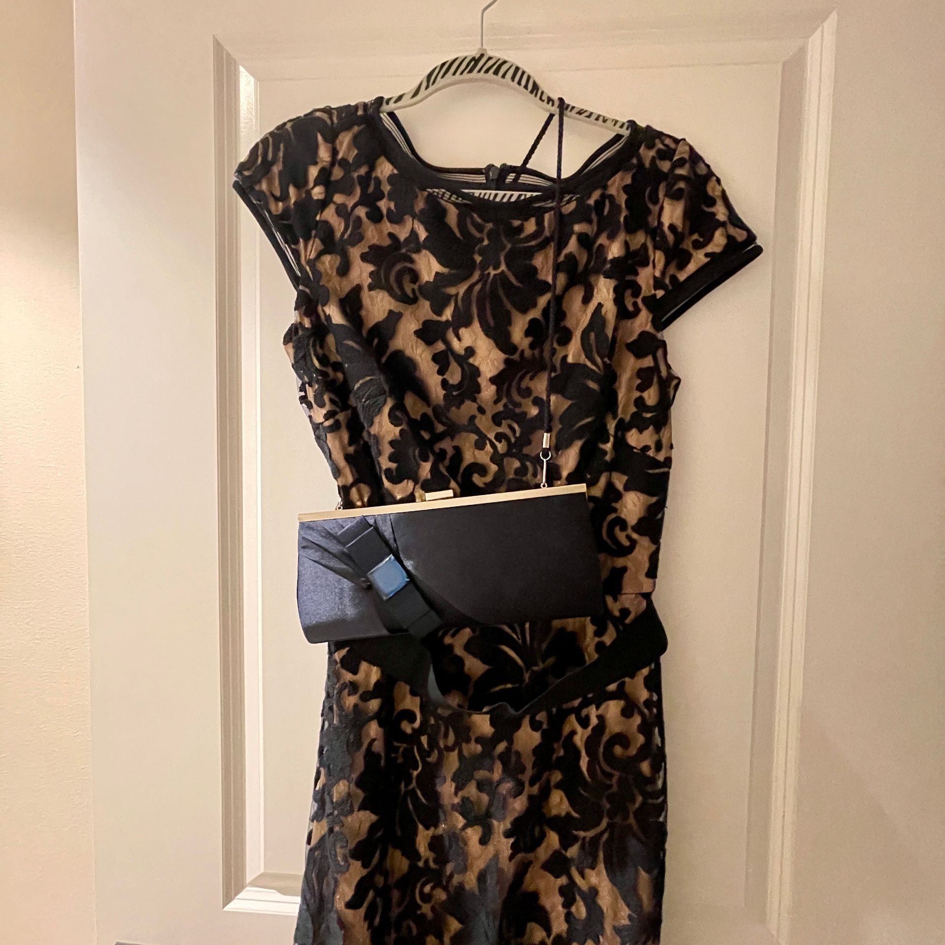 Black lace dress with gold lining and navy blue clutch hanging on a white door.