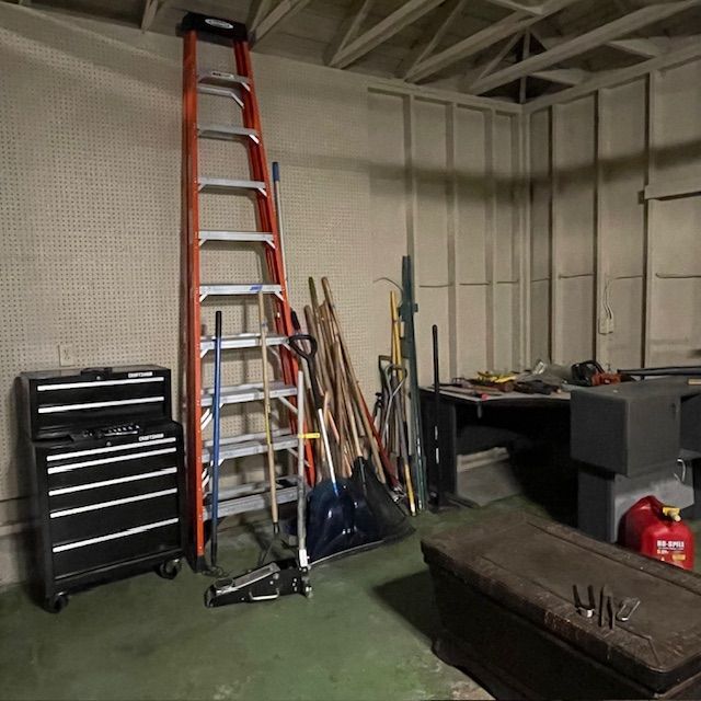 A cluttered workshop with tools, a ladder, toolbox, and a red gas can.