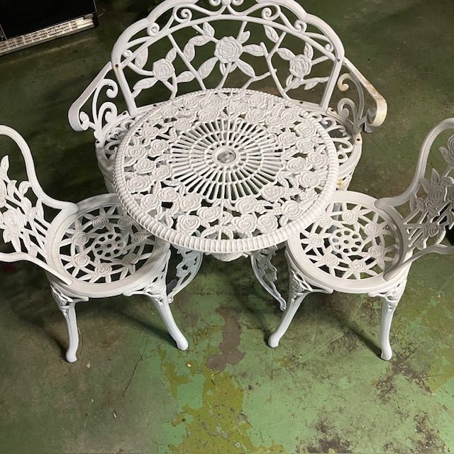 White ornate metal patio furniture set: table and three chairs with floral detailing.