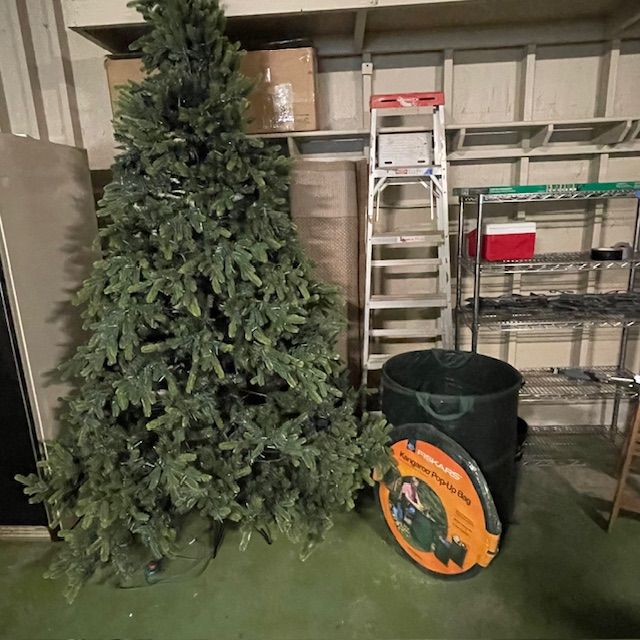 Artificial Christmas tree, ladder, storage container, and shelves in a storage room.