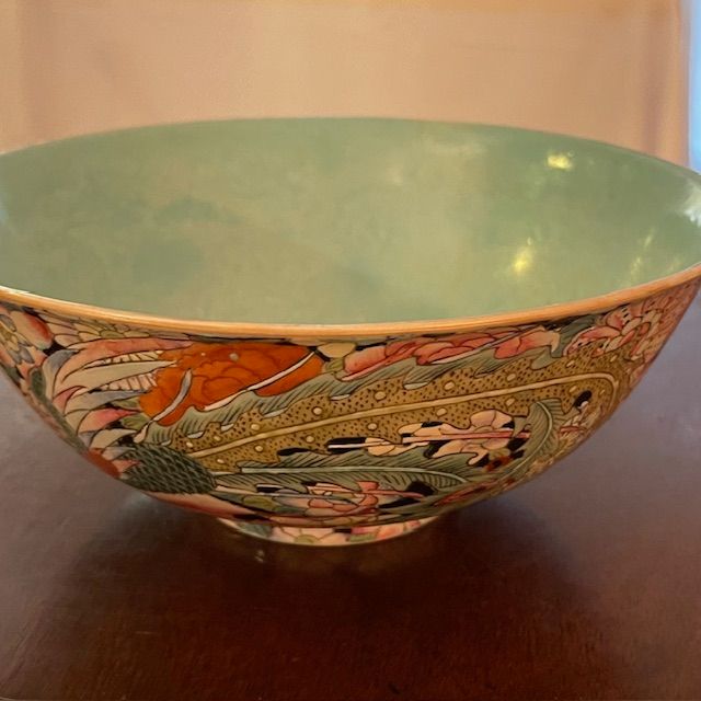 Colorful floral patterned porcelain bowl with a light green interior on a brown surface.