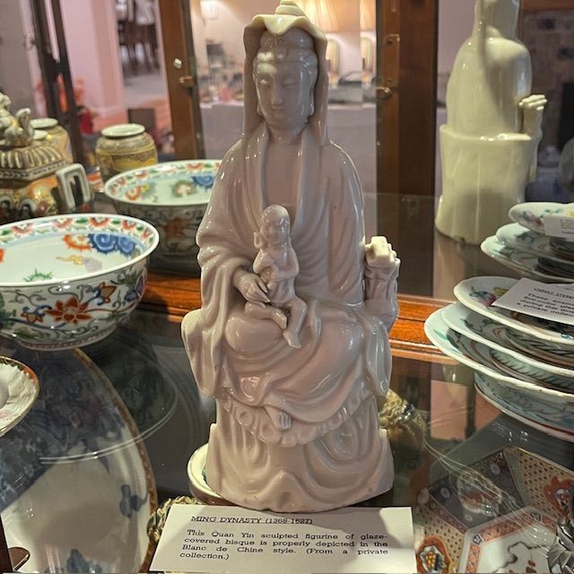 Porcelain statue of a woman holding a child, displayed in a glass cabinet.