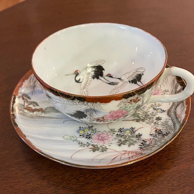 Delicate teacup and saucer with a painted Japanese landscape featuring cranes and floral details.