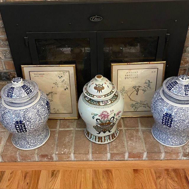 Fireplace mantel with blue and white jars, a center jar, and two framed pictures.