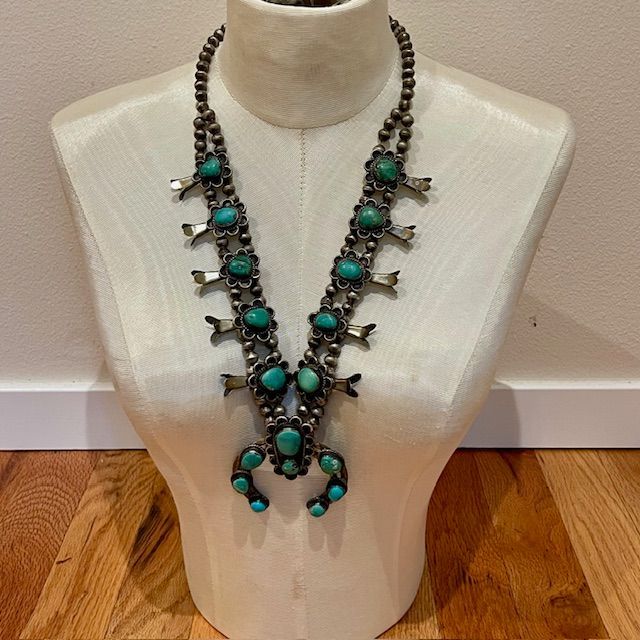 Turquoise squash blossom necklace on a white mannequin.