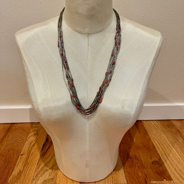 Multi-strand necklace with red beads on a bust form.