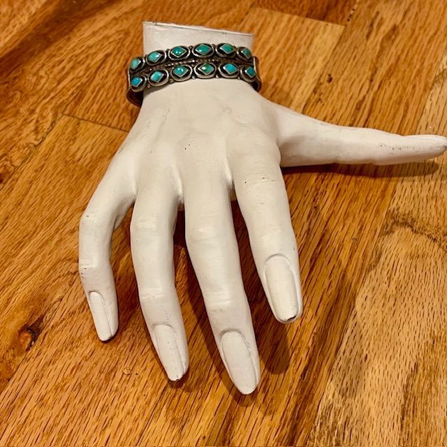 A white mannequin hand displays a turquoise bracelet on a wood surface.
