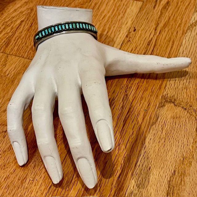 White hand mannequin with turquoise and silver bracelet on a wood surface.