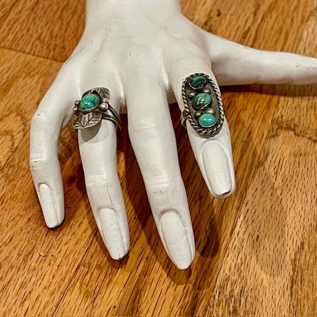 Two turquoise stone rings on a white hand-shaped display, set on a wood surface.