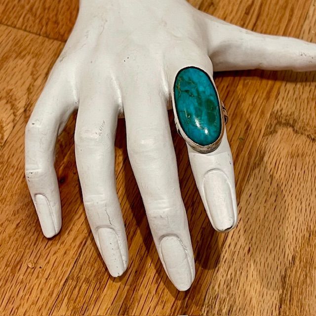 White hand with a large turquoise ring on a wooden surface.
