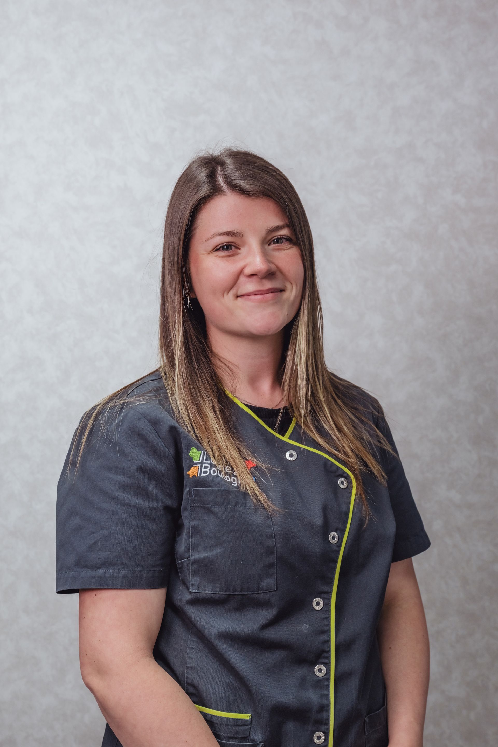 Une femme en uniforme bleu sarcelle foncé sourit à l'objectif, sur fond clair.