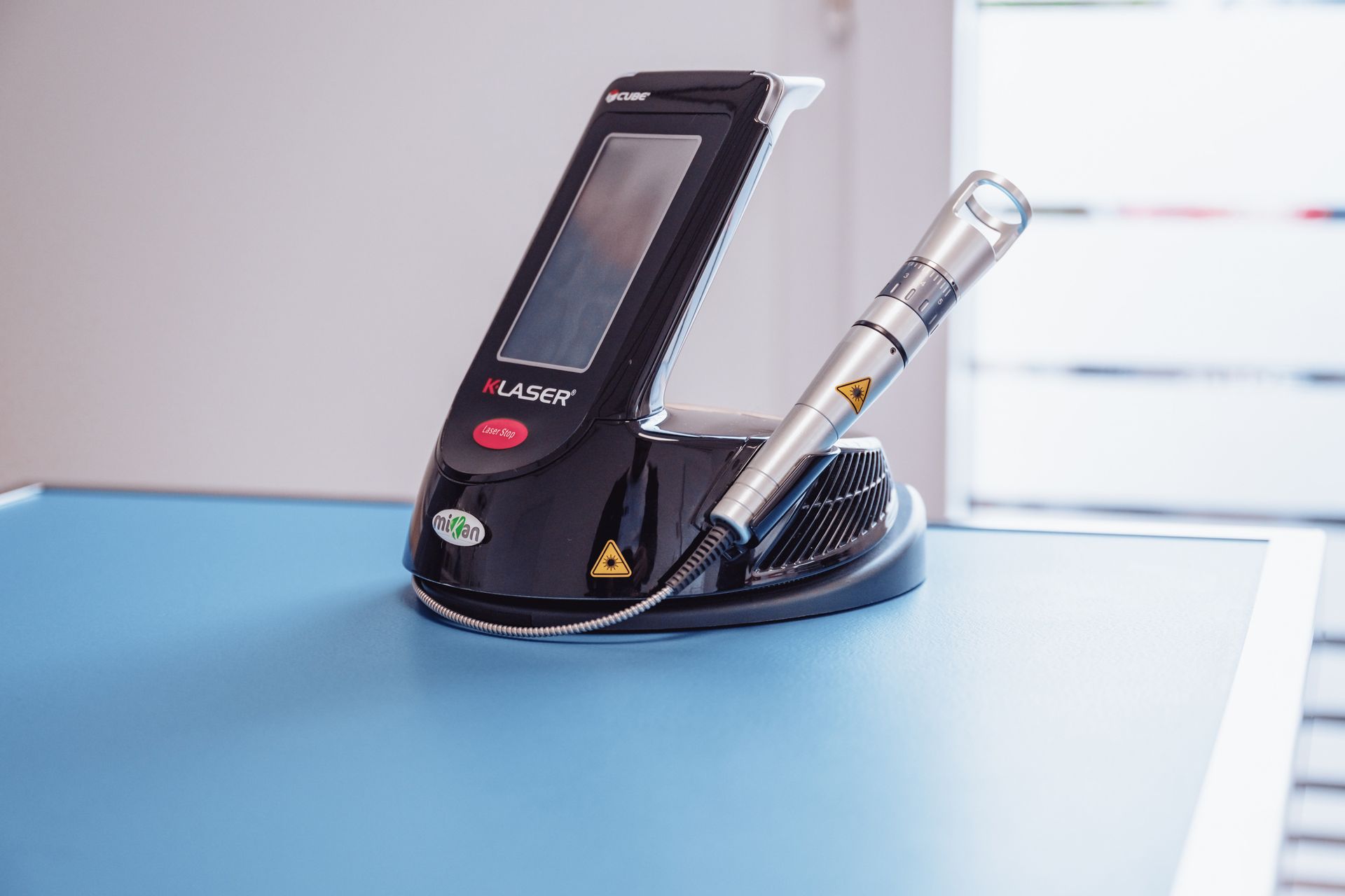 Appareil laser sur une table bleue, avec un panneau de commande noir et une pièce à main argentée, à l'intérieur.