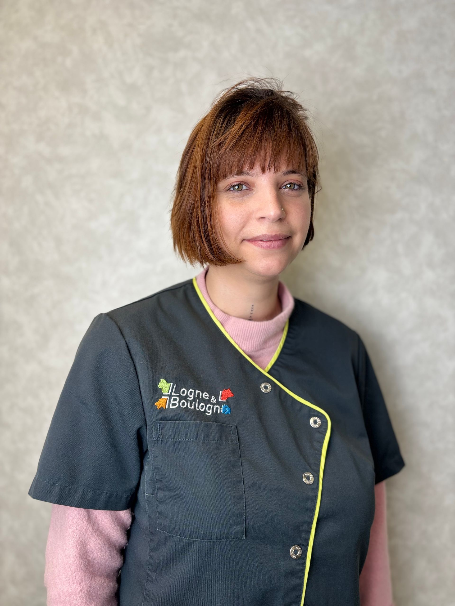 Femme souriante en blouse blanche et chemise rouge, cheveux bruns coiffés en chignon.