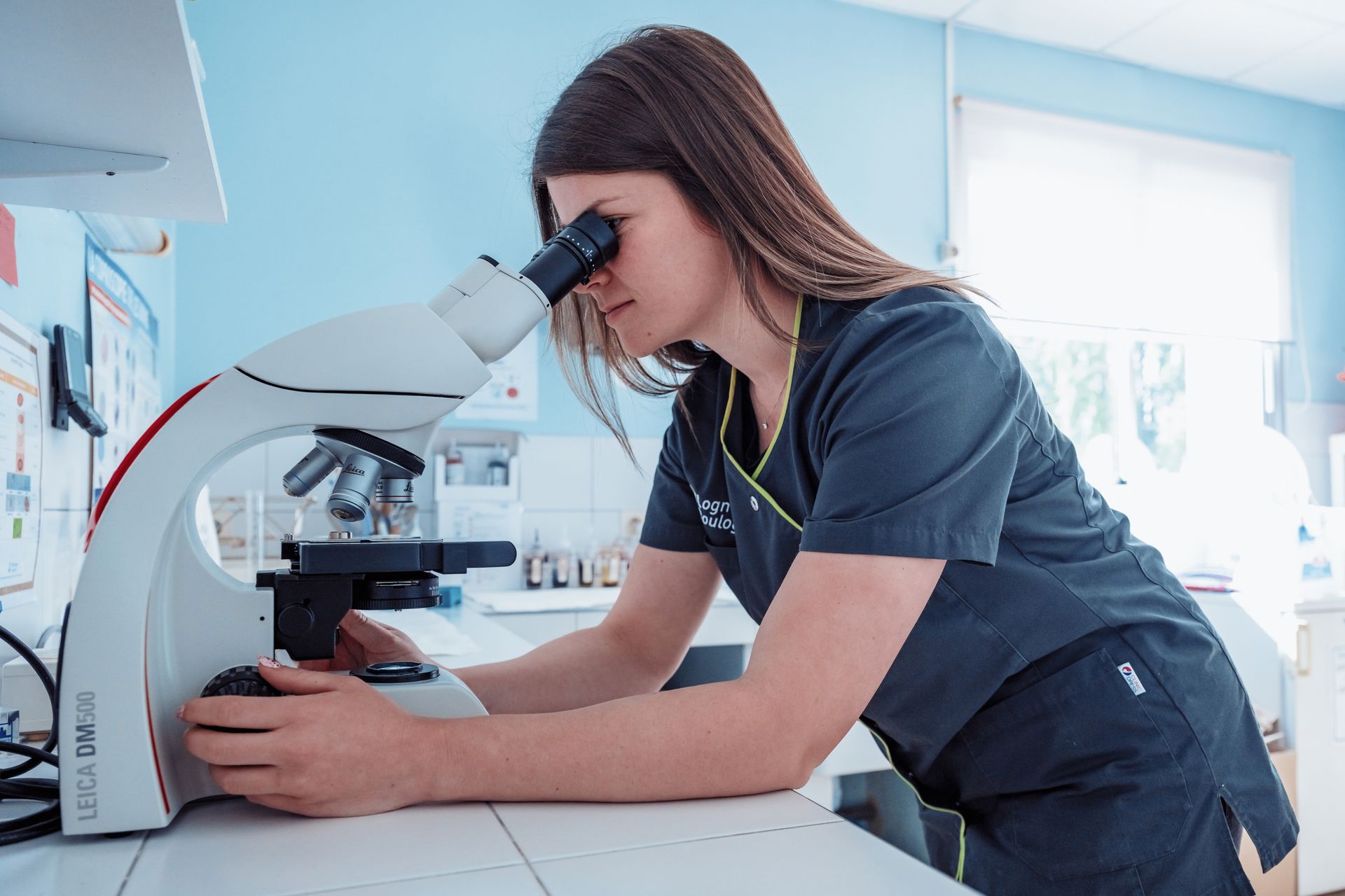 Femme en blouse médicale observant au microscope dans un laboratoire vétérinaire.