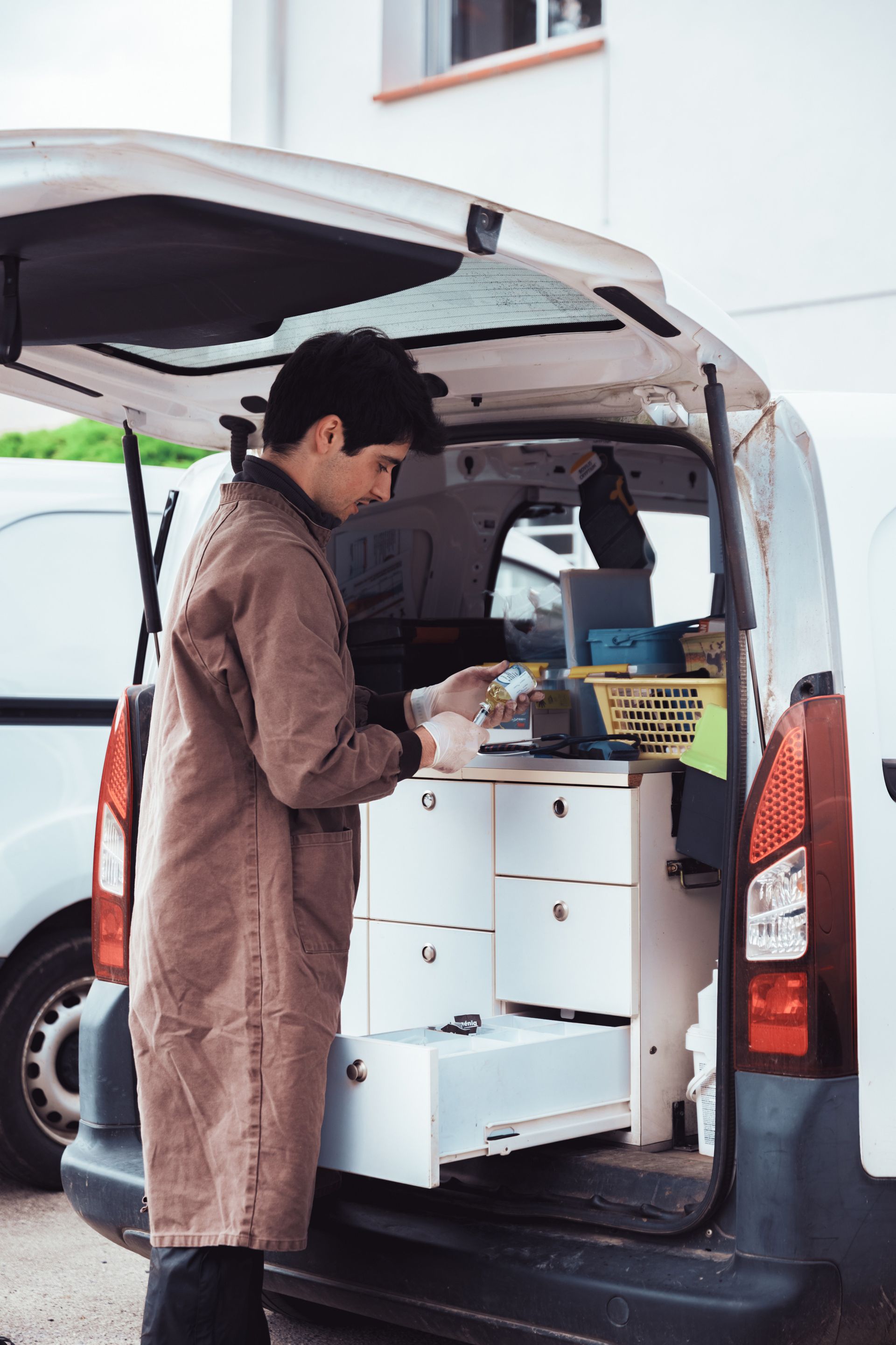 Une personne en manteau marron se tient à l'arrière d'une camionnette et regarde à l'intérieur des tiroirs.