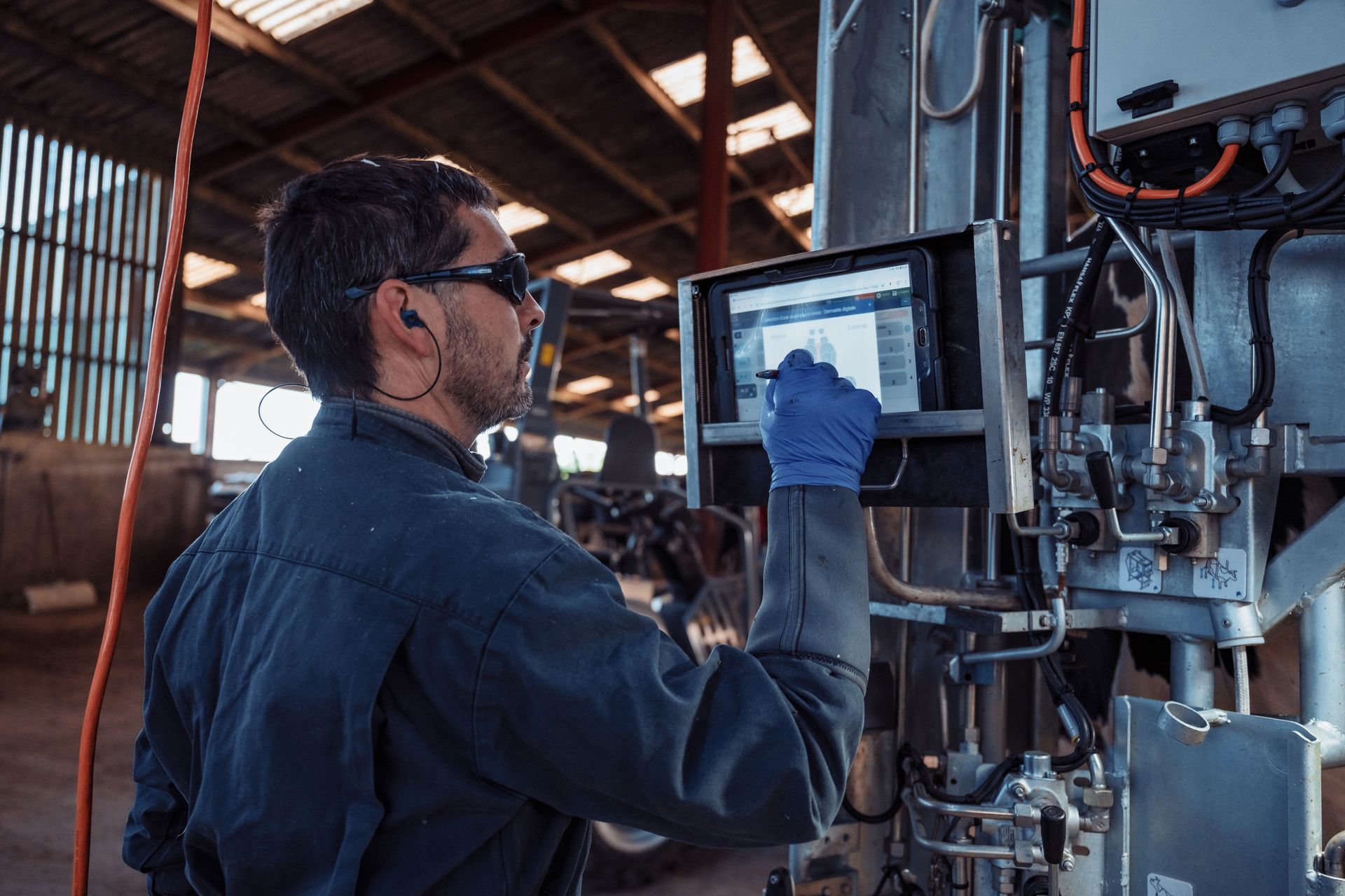 Un homme portant des gants et une chemise bleus actionne un panneau de commande tactile sur un équipement industriel dans une grange.