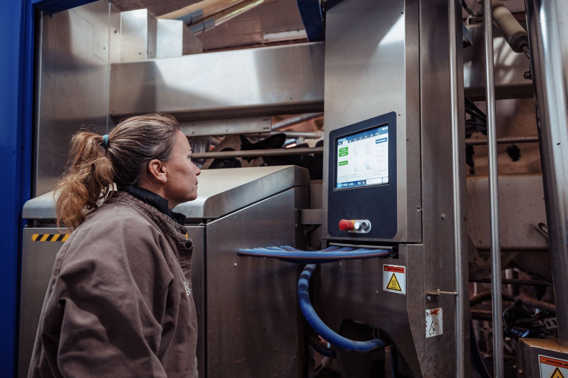 Une femme regarde l'écran d'une machine en acier inoxydable dans un environnement industriel aux murs bleus.