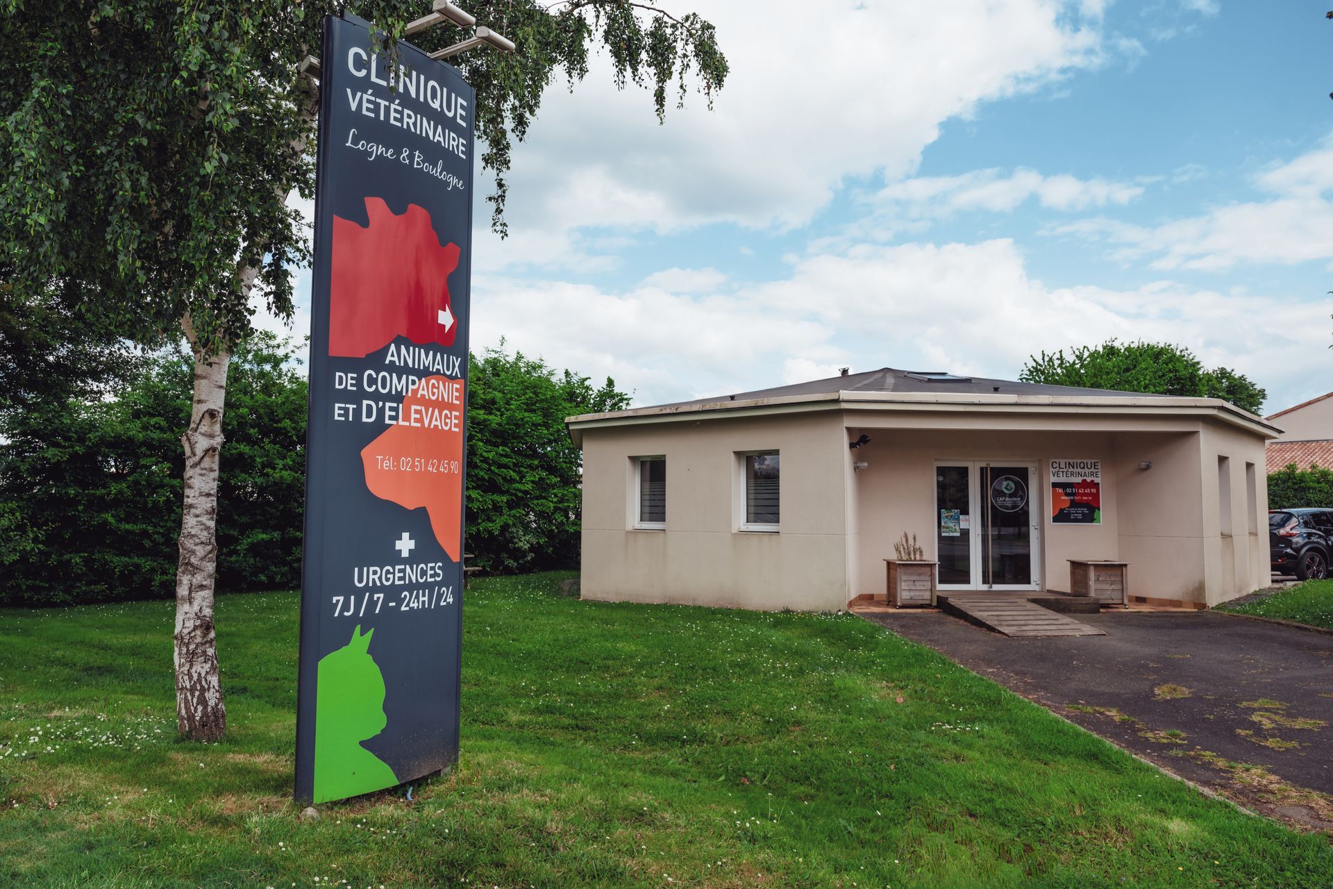 Extérieur d'une clinique vétérinaire avec une enseigne et un bâtiment sur une pelouse. L'enseigne comporte des formes et du texte colorés.