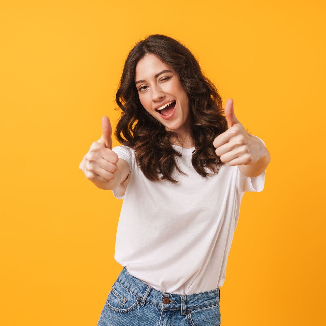 A young woman is giving a thumbs up sign over a yellow background.