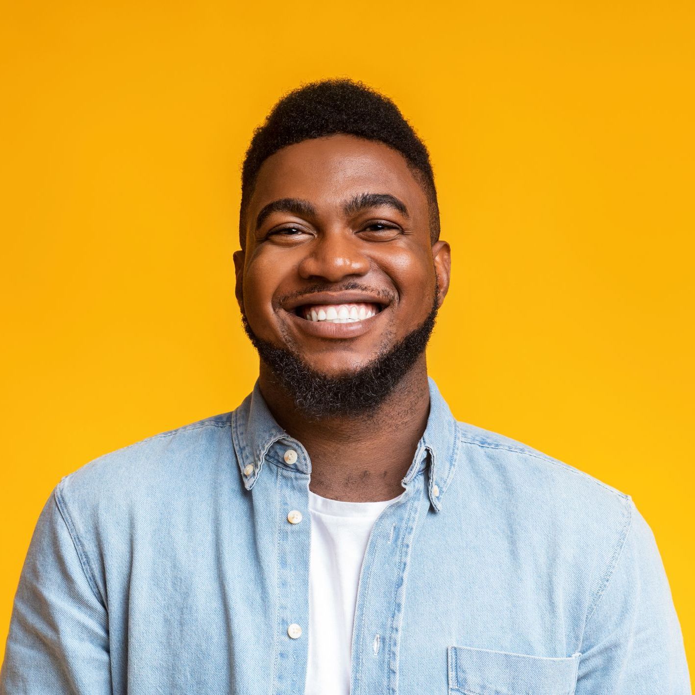 A man with a beard is smiling in front of a yellow background.