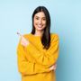 A woman in a yellow sweater is smiling and pointing to the side.