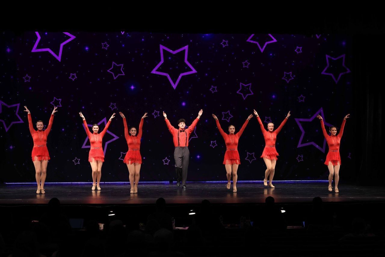 A group of dancers are performing on a stage with purple stars in the background.