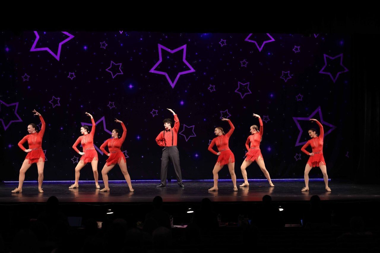 A group of dancers are performing on a stage with purple stars in the background.