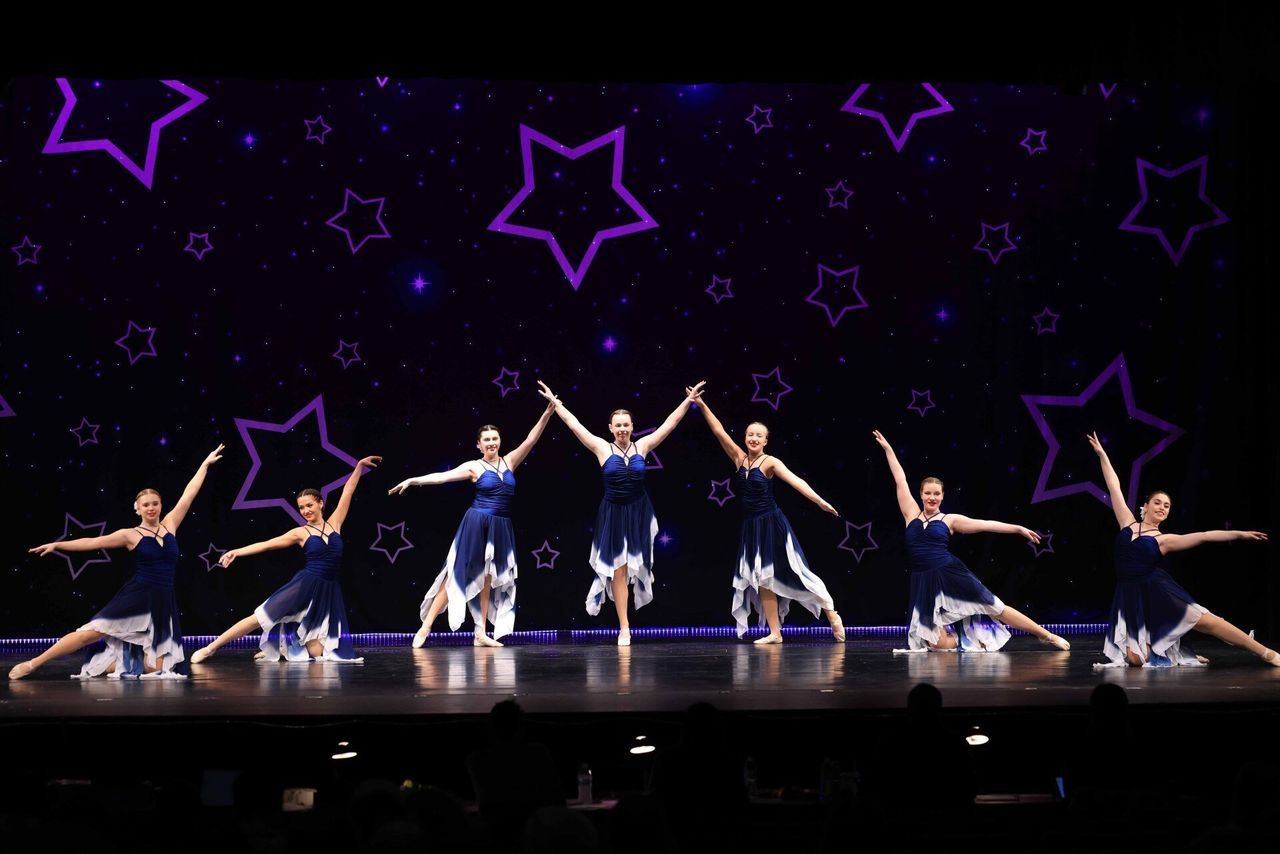 A group of dancers are performing on a stage with purple stars in the background.