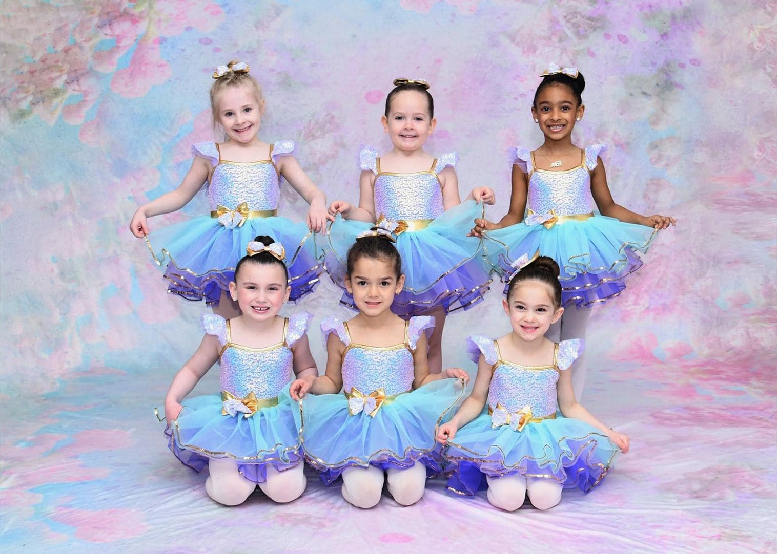 A group of young girls in blue and purple tutus are posing for a picture.