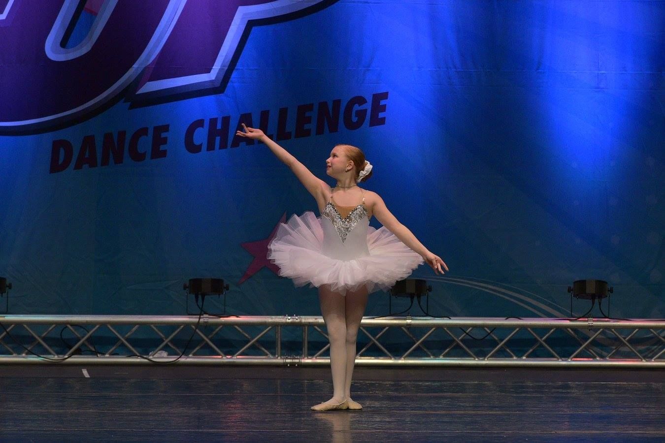 A little girl in a tutu is dancing in stage.