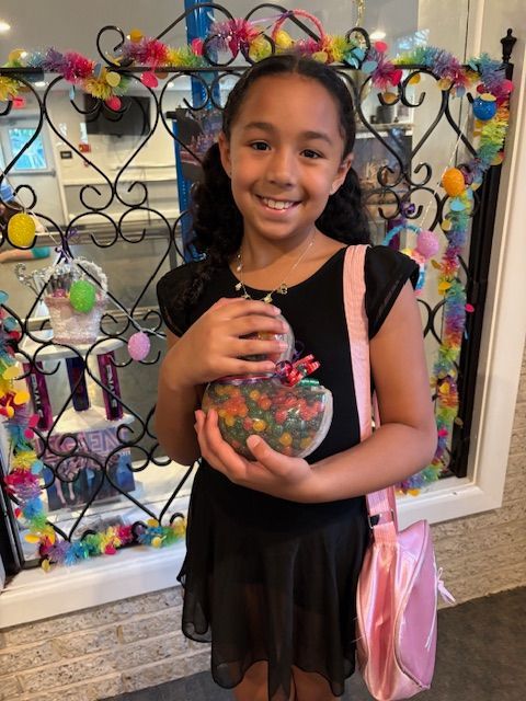 Girl smiling and holding a colorful craft heart in front of a decorative display wall
