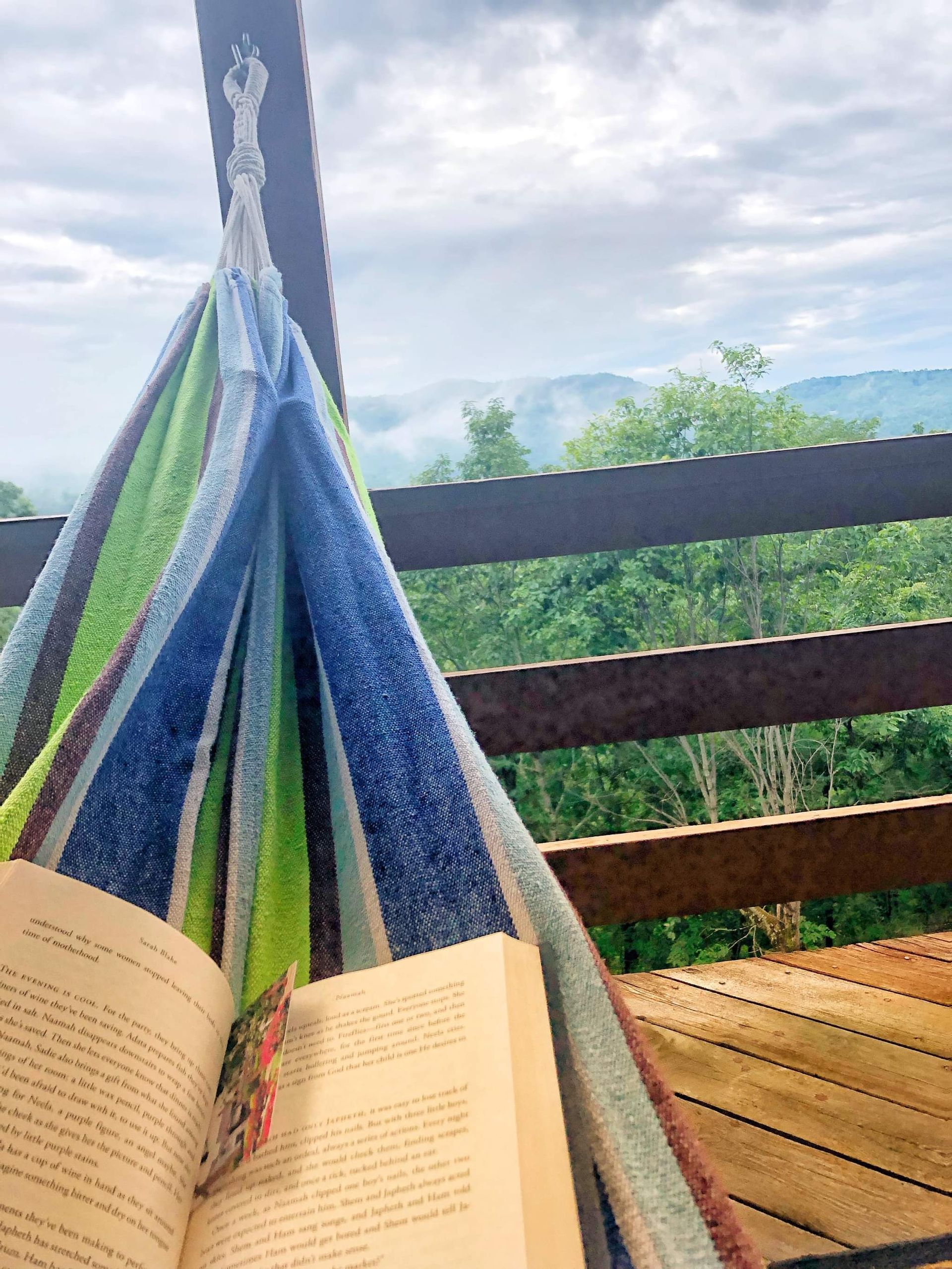 Hammock with open book on a deck overlooking a foggy forest.