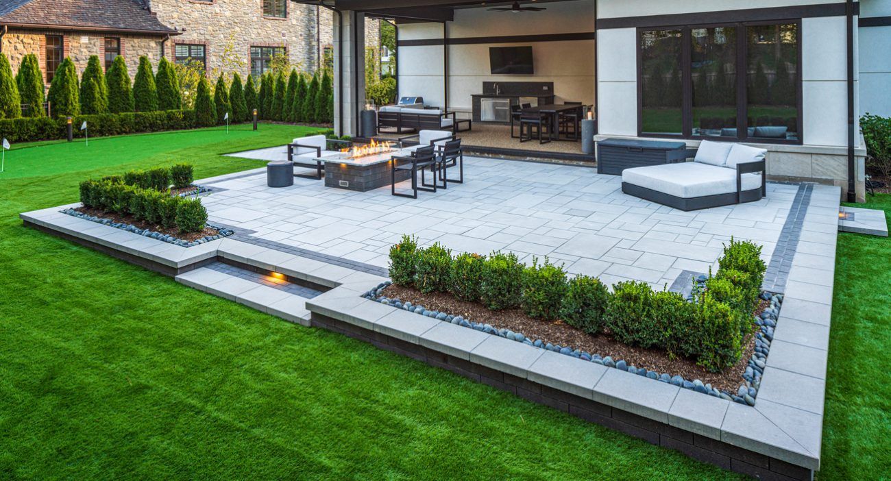 A large patio with a fire pit , chairs , and a table in the backyard of a house.