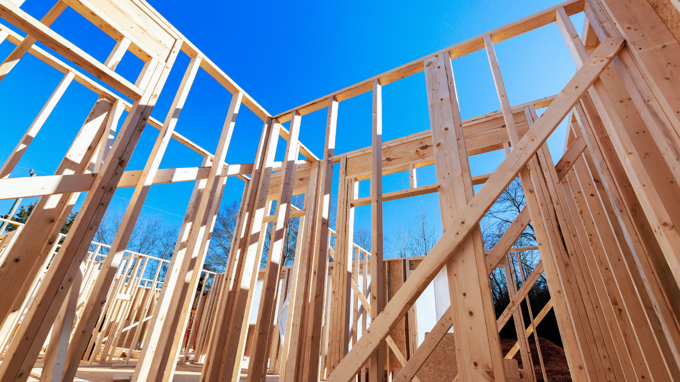 Wooden frame of a building under construction against a bright blue sky.