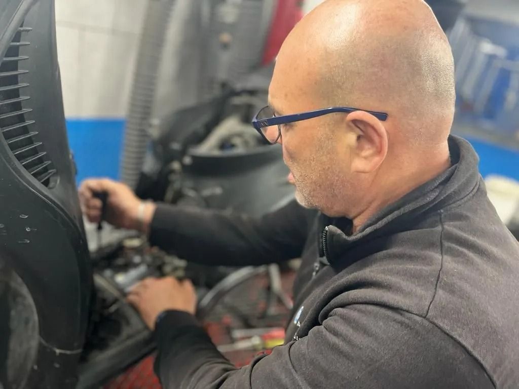 Meccanico con gli occhiali che lavora sul motore, giacca nera, ambiente da garage.