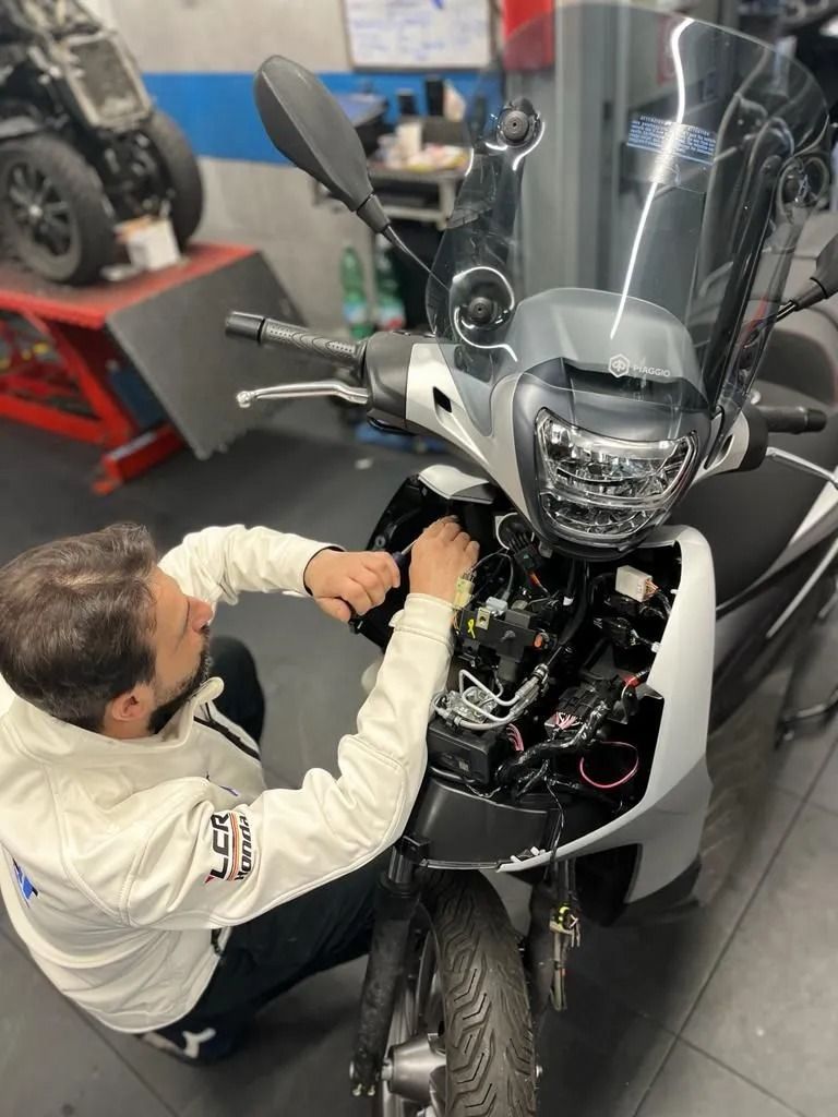 Meccanico al lavoro sulla parte anteriore di uno scooter argentato in un'officina.