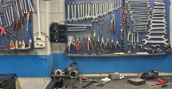 Attrezzi da officina organizzati su pannelli forati; un banco da lavoro con parti di motore. Toni blu e grigi.