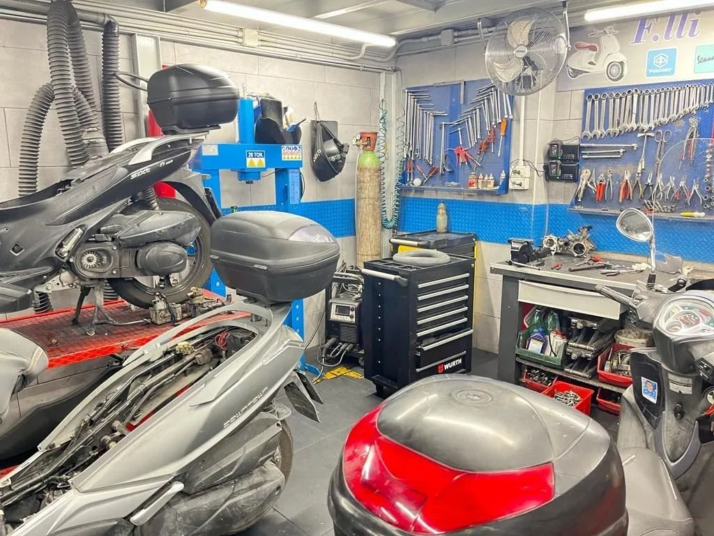 Officina di riparazione motociclette, diverse moto in riparazione, attrezzi sul muro.