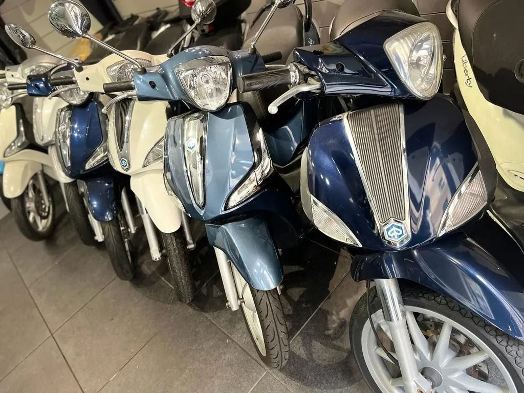 Fila di scooter blu e bianchi parcheggiati al chiuso.