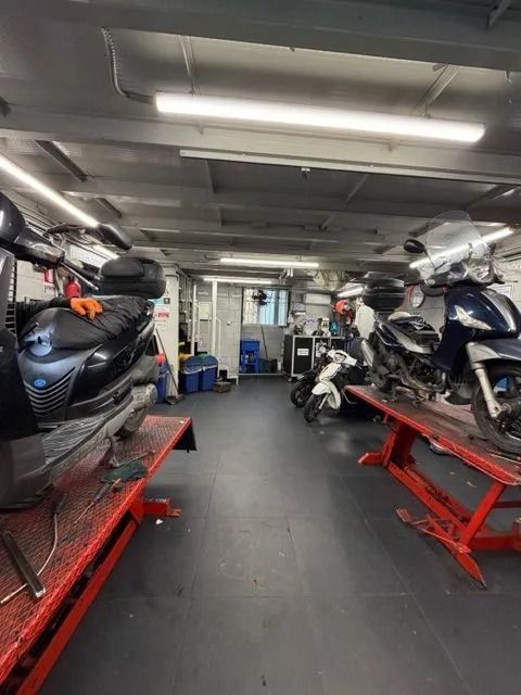 Officina per la riparazione di motociclette con scooter su ponti sollevatori. Illuminazione fluorescente, attrezzi e un piccolo ufficio.