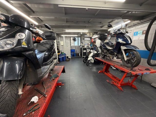 Officina per la riparazione di motociclette con due scooter su ponti sollevatori, attrezzi e altre moto visibili.