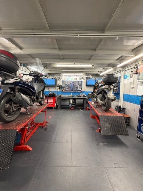 Due scooter su sollevatori rossi all'interno di un'officina di riparazione scooter con attrezzi e banchi da lavoro.