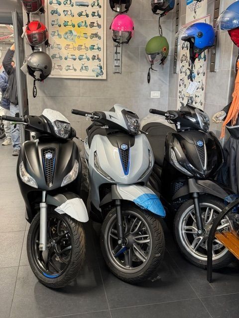 Tre scooter esposti in un negozio, con i caschi appesi sopra.